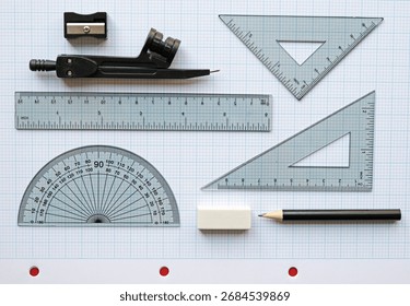 Back to or return to school geometry, maths or technical drawing set. Plastic triangle, ruler angle measurement hemisphere, eraser or rubber compass, pencil and sharpener. On graph paper. Flat lay