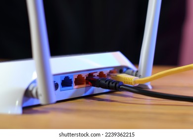 back of router with ethernet ports and connected cables on wooden table - Shutterstock ID 2239362215