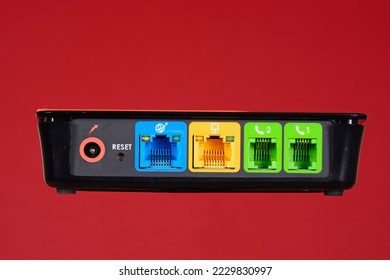 The back of a router unit showing internet, computer and phone line sockets against a red background, UK. - Shutterstock ID 2229830997