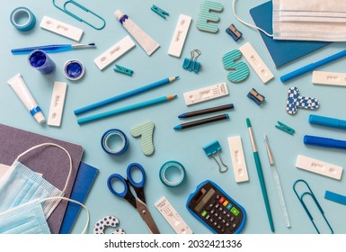 Back To School 2021, Covid 19 Days. Student Supplies And Coronavirus Spread Prevention Measures Flat Lay. Rapid Self Test, Protective Medical Mask And Stationery On Blue Background, Top View