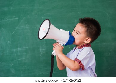 Back To School. Asian Funny Cute Little Child Boy Kindergarten Preschool In Student Uniform Speaking Through Megaphone Against On Green School Blackboard, First Time To School Education Concept