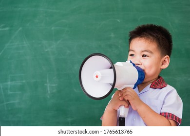 Back To School. Asian Funny Cute Little Child Boy Kindergarten Preschool In Student Uniform Speaking Through Megaphone Against On Green School Blackboard, First Time To School Education Concept