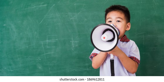 Back To School. Asian Funny Cute Little Child Boy Kindergarten Preschool In Student Uniform Speaking Through Megaphone Against On Green School Blackboard, First Time To School Education Concept