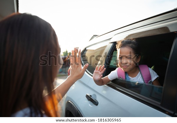 Back to\
school. Asian pupil girl with backpack sitting in the car waving\
goodbye to her mother to get ready to\
school.
