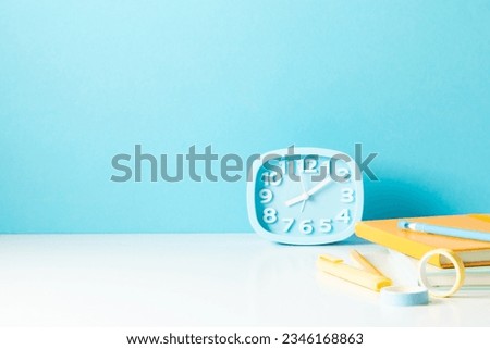 Back to school background. School accessories, notebook, pens, alarm clock on pastel blue wall background. Education, studing and back to school concept. Front view