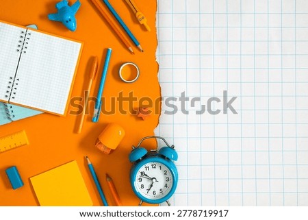 Back to school background featuring blue alarm clock, open notebook, pencils, and vibrant stationery tools flat lay on bright orange torn paper over blank checkered layout with ample copy space.