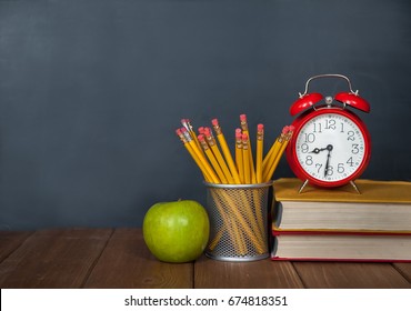 Back to school background on wooden table and blackboard on a background. Books, pencils, alarm clock and apple on desk. First time to school. Elementary school - Powered by Shutterstock