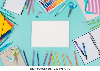 Back to school background. Top view to school stationery, books, notebooks, pencils, pen, watercolor paint on green background. Open white spiral sketchbook notebook in the middle