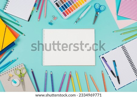 Back to school background. Top view to school stationery, books, notebooks, pencils, pen, watercolor paint on green background. Open white spiral sketchbook notebook in the middle