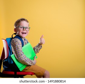 Back To School. Child Boy Sitting On School Chair And Pointing Up. Exciting And Wondering Kid. Student Of Primary School In Glasses. 