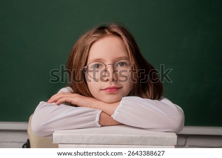 Back to school. Child holding stack of books with mortar board on blackboard. School girl. School child. Portrait of elementary pupil. Happy schoolgirl. Schoolkid or preschooler
