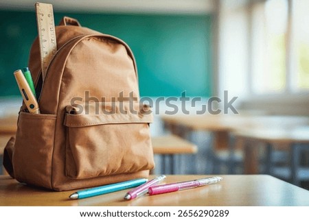 Back to school concept — school backpack with educational supplies placed on wooden desk in  bright classroom. Empty space in the foreground for placing product or text.