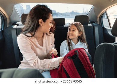 Back to school concept. Beautiful mother checking daughter backpack, sitting with child girl on back seat in car, riding to school in the morning - Powered by Shutterstock