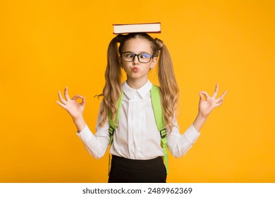 Back To School Concept. Cute Nerdy Schoolgirl Meditating With Book On Head On Yellow Studio Background. Free Space - Powered by Shutterstock