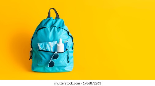 Back To School Concept During Corona Pandemic. Schoolbag With Medical Masks, Disinfectant And Pencils Isolated On Yellow Background. New School Rules