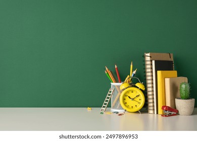 Back to school concept featuring colorful pencils, yellow alarm clock, notebooks, and stationery on a white desk against green background - Powered by Shutterstock