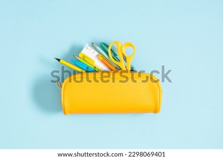 Back to school concept. Flat lay top view on yellow full pencil case with pencils and pens notepad scissors isolated on pastel blue background