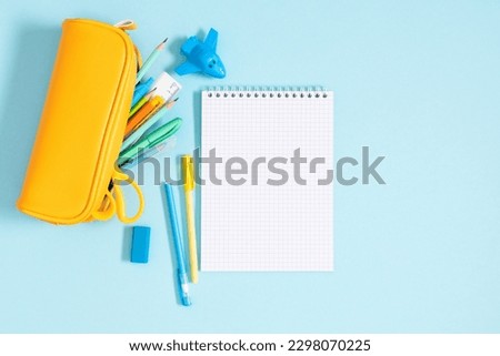 Back to school concept. Flat lay top view on yellow full pencil case with pencils and pens notepad scissors isolated on pastel blue background