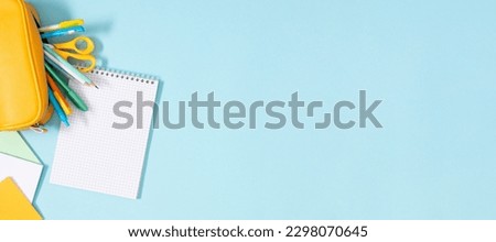 Back to school concept. Flat lay top view of on a yellow full pencil case with pencils and pens notepad scissors paper for notesisolated on pastel blue backgroun banner
