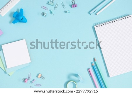 Back to school concept. Flat lay top view of scattered stationery notepad pens pencils paper clips airplane sticky tape note paper isolated on pastel blue background
