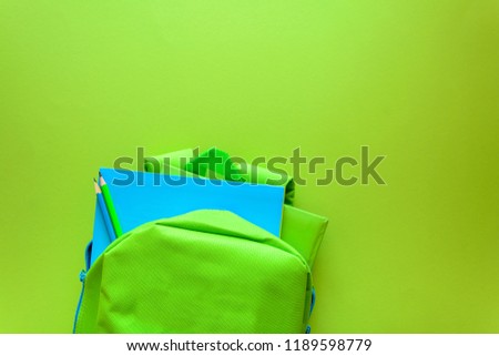 Back to school concept. Green backpack with school supplies on green background. Top view. Copy space