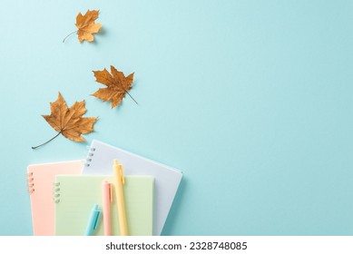 Back to school concept. High angle view creative photo featuring colorful notebooks and pens with maple leaves on calming pastel blue background with copy-space for text or advertisements - Powered by Shutterstock