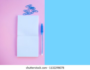 Back to school concept. Noteblock, pen and paper clip on pink and blue background with text space.