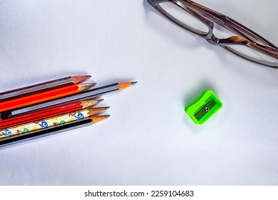 Back to school concept- a Pencil,erasor, sharpner an cut foil of the pencil on white table with or without spectacles not properly aranged isolated.