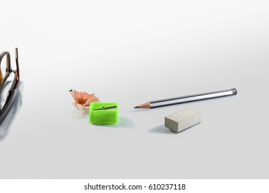Back to school concept- a Pencil,erasor, sharpner an cut slice of the pencil on white table with or without spectacles not properly aranged isolated.