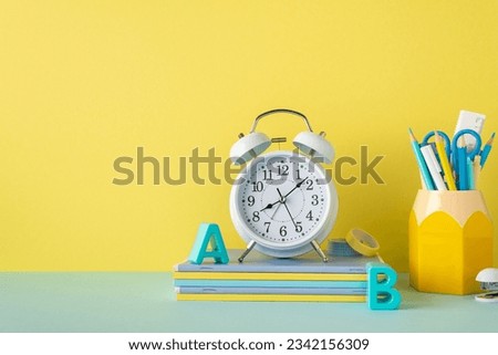 Back to school concept. Photo of school accessories on blue desktop alarm clock plastic alphabet letters stack of notepads adhesive tape stapler and stand for pens on yellow wall background
