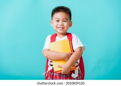 Back To School Concept. Portrait Asian Happy Funny Cute Little Child Boy Smiling And Laugh Hug Books, Studio Shot Isolated Blue Background. Kid From Preschool Kindergarten With School Bag Education