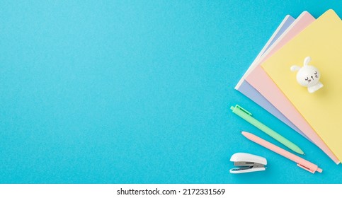 Back to school concept. Top view photo of colorful stationery stack of notepads bunny shaped sharpener mini stapler and pens on isolated blue background with copyspace