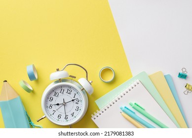 Back to school concept. Top view photo of school supplies alarm clock colorful notebooks pencil-case pens binder clips and adhesive tape on bicolor yellow and white background