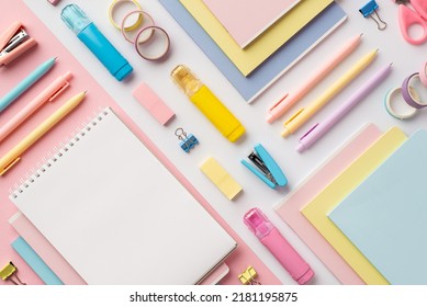 Back to school concept. Top view photo of colorful stationery copybooks pens staplers binder clips correctors erasers and adhesive tape on bicolor white and pink background with blank space