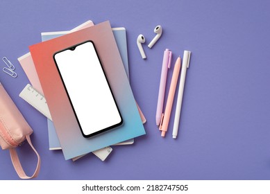 Back to school concept. Top view photo of smartphone over colorful diaries earbuds pens ruler clips and pink pencil-case on isolated purple background with blank space