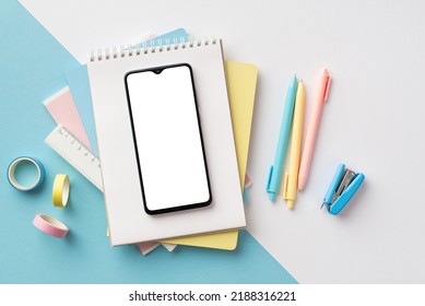 Back to school concept. Top view photo of school supplies smartphone over notebooks pens ruler stapler and adhesive tape on bicolor blue and white background with copyspace