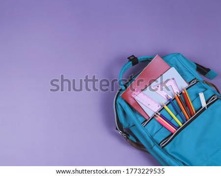 Back to school concept.Top view of backpack with school supplies on purple background with copy space.