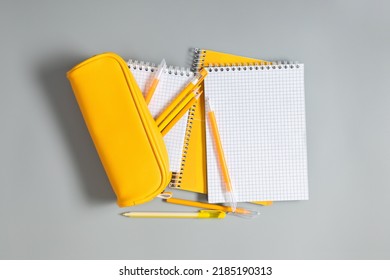 Back to school concept. Yellow school pencil case with filling school stationery, notebook, pens, pencils. Yellow school accessories on grey background. Flat lay, top view, copy space