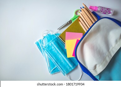 Back To School During Pandemic. Top View Of School Desk With Face Mask, Supplies And Accessories. School Supplies And COVID 19 Prevention Items. Back To School During Pandemic Concept.