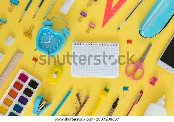 Back to school. Education concept. Everything for\
school and office. School supplies. Pens, alarm clock, pencils,\
notebook, glasses and everything for study on a yellow background.\
Flatly. From above.