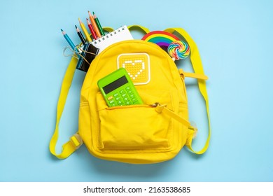 Back to school, education concept Yellow backpack with school supplies - notebook, pens, eraser rainbow, numbers isolated on blue background Top view Copy space Flat lay composition