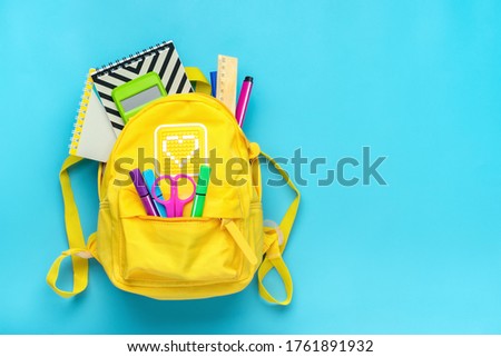 Back to school, education concept. Yellow backpack with school supplies - notebook, pens, ruler, calculator, scissors isolated on blue background. Top view. Copy space Flat lay composition