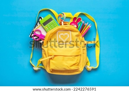 Back to school, education concept Yellow backpack with school supplies - notebook, pens, eraser rainbow, numbers isolated on blue background Top view Copy space Flat lay composition
