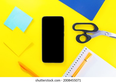 Back to school. Education flat lay. Business layout. Mobile phone mock up, notepad, pen, sticker paper, scissors on yellow background. Copy space