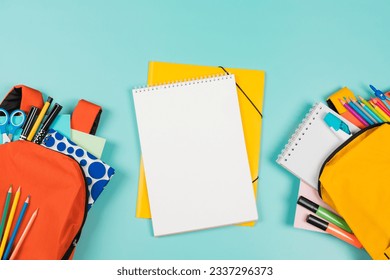 Back to school, education, learning concept. Two open backpacks with school supplies and open white spiral sketchbook notebook on pastel green background. Top view - Powered by Shutterstock