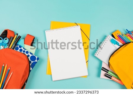 Back to school, education, learning concept. Two open backpacks with school supplies and open white spiral sketchbook notebook on pastel green background. Top view