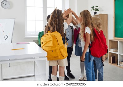 Back to school. Elementary students meet at school, interact with each other, make new friends, form bonds. Group of children with backpacks standing in circle and putting their hands together - Powered by Shutterstock