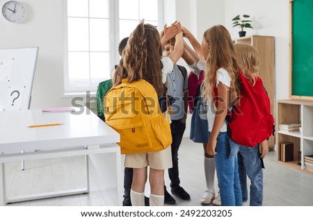 Back to school. Elementary students meet at school, interact with each other, make new friends, form bonds. Group of children with backpacks standing in circle and putting their hands together