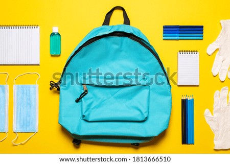 Back to school flat lay with face masks, gloves,  hand sanitizer, and school supplies. Blue backpack, hygiene objects, and school supplies isolated on a yellow background.