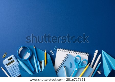Back to school flat lay featuring blue stationery, notebook, pencil, scissors, calculator and magnifier on a deep blue background conveying education, study and classroom preparation